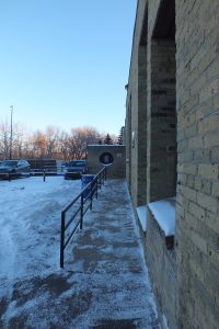 Une rampe avec une balustrade menant à un immeuble en briques de couleur pâle à partir d'un stationnement.
